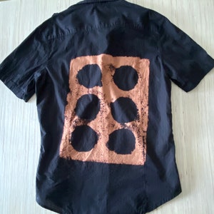 May include: Black short-sleeved button-down shirt with a brown rectangular design featuring six circles.