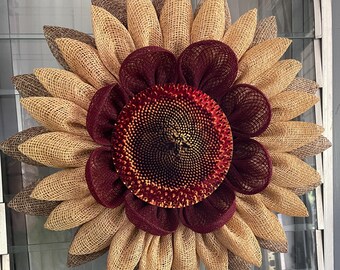 May include: A large burlap sunflower wreath with a burgundy center. The sunflower has a brown and tan burlap texture.