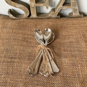 May include: Four silver spoons tied together with twine, resting on a brown hessian surface.