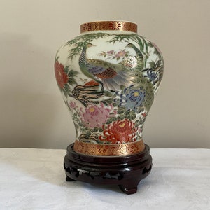 Peut inclure: Un vase en porcelaine blanche avec un motif floral et de paon. Le vase est sur un piédestal en bois foncé.