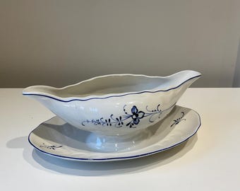 May include: White ceramic gravy boat with a matching saucer. The set features a blue floral design and a scalloped edge. The gravy boat has a spout and handle. A classic addition to any dining table.