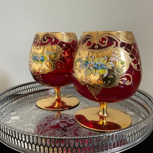 Può includere: Due calici di vetro rosso con disegni floreali dipinti in oro e bianco su un vassoio d'argento.