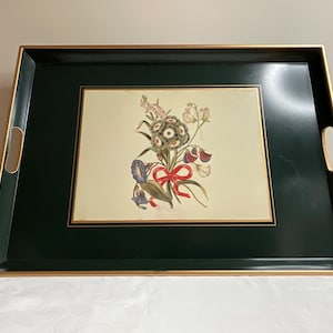 May include: Rectangular serving tray with a dark green border and gold trim. The center features a floral illustration with a red bow. The tray has cut-out handles on each side, offering a decorative and functional design.