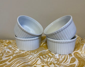 May include: Four white ceramic ramekins stacked on top of each other. The ramekins have a fluted design and are perfect for baking individual desserts.