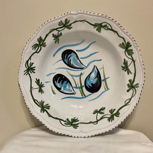 Op de afbeelding: Witte keramische soepkom met een groene wijnstokrand en blauw-zwarte geverfde mosselen.