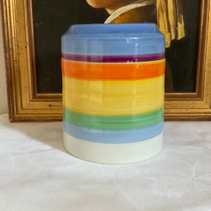 May include: A ceramic vase with a blue, white, yellow, orange, green and purple striped pattern.