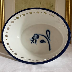 May include: White oval serving bowl with a blue floral design. The bowl has a dark blue rim and a decorative pierced edge. The floral design is a stylized blue flower on a stem.