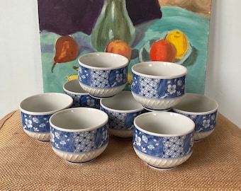 Könnte beinhalten: Ein Set aus acht Keramik-Teetassen. Jede Tasse hat einen weißen Innenraum und ein blau-weißes Blumen- und geometrisches Muster auf der Außenseite. Die Tassen sind auf einer Jutefläche angeordnet.