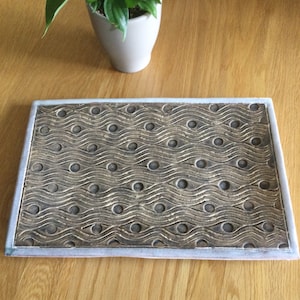 May include: A rectangular ceramic tray with a wavy pattern and small circles embossed in the surface. The tray is a light brown colour with a white border.