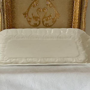 May include: A white ceramic serving tray with a decorative, raised floral design around the edge.