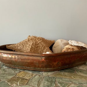 May include: A hammered copper bowl filled with seashells, including a starfish and a sand dollar. The bowl is oval shaped and has a rustic, antique look.