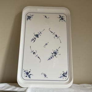 May include: A rectangular white serving tray with rounded corners, featuring a delicate blue floral pattern. The design includes small flower clusters in the corners and center, connected by thin, curved blue lines on a smooth surface.