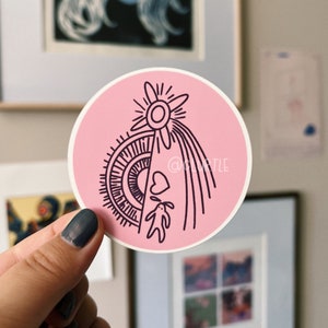 Puede incluir: Pegatina rosa con una ilustración en blanco y negro de una estrella con un corazón y un conejo. La estrella tiene un círculo en el centro y rayos de luz que salen de ella. El corazón está debajo de la estrella y el conejo debajo del corazón.