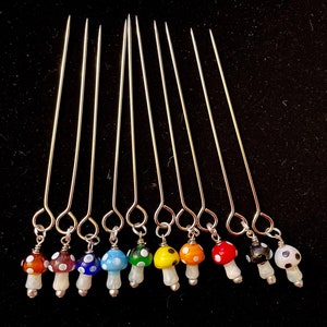 May include: Ten silver knitting needles with colorful mushroom-shaped beads attached to the ends. The beads are red, orange, yellow, green, blue, purple, black, and white.