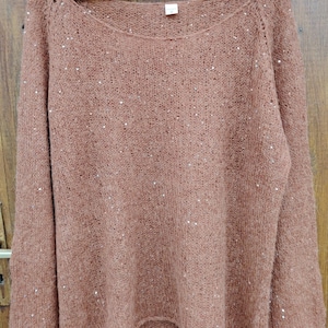 Puede incluir: Un suéter marrón con lentejuelas, mangas largas y un corte holgado.