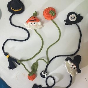May include: A collection of five handmade crochet bookmarks featuring Halloween-themed designs including a black witch hat, a white ghost wearing a pumpkin hat, a small orange pumpkin, a white ghost with a black hood, and a black star with a white center.