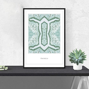 Può includere: Una stampa incorniciata con un design astratto verde e bianco. Il design è simmetrico e ricorda una figura umana. Il testo "formica" è stampato sotto il design.