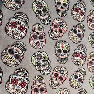 May include: A gray fabric with a repeating pattern of colorful sugar skulls. The skulls are decorated with flowers and other designs.