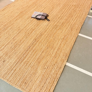 K&ouml;nnte beinhalten: Ein Naturfaser-Teppich aus Jute, einem nachhaltigen und strapazierf&auml;higen Material. Der Teppich hat eine hellbraune Farbe und eine gewebte Textur. Er ist perfekt, um jedem Raum einen Hauch von nat&uuml;rlicher Sch&ouml;nheit zu verleihen.