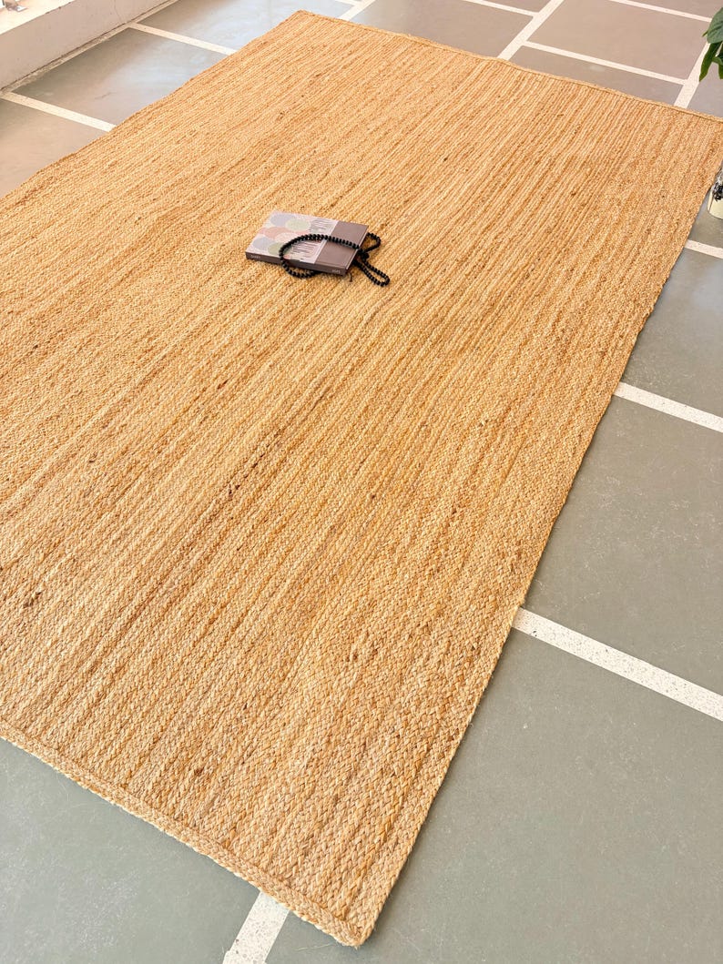 K&ouml;nnte beinhalten: Ein Naturfaser-Teppich aus Jute, einem nachhaltigen und strapazierf&auml;higen Material. Der Teppich hat eine hellbraune Farbe und eine gewebte Textur. Er ist perfekt, um jedem Raum einen Hauch von nat&uuml;rlicher Sch&ouml;nheit zu verleihen.
