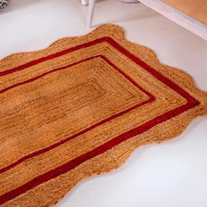 May include: A rectangular jute rug with a scalloped edge and a double red border. The rug is made of natural fibers and has a rustic, earthy look.