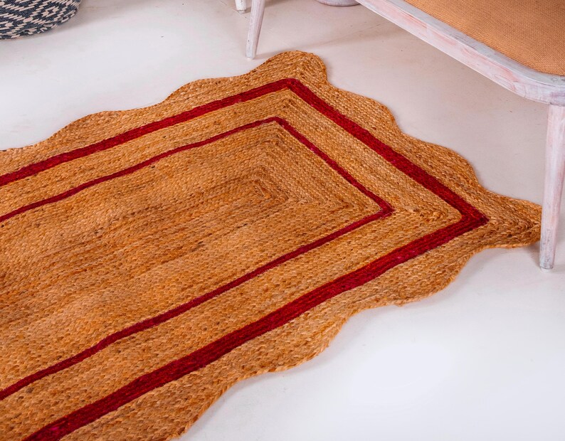 May include: A rectangular jute rug with a scalloped edge and a double red border. The rug is made of natural fibers and has a rustic, earthy look.