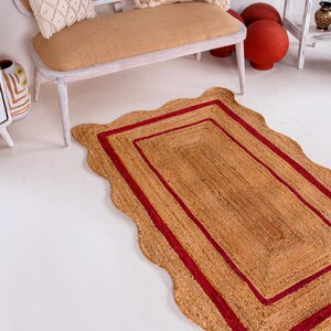May include: A rectangular jute rug with a scalloped edge and two red stripes around the border.