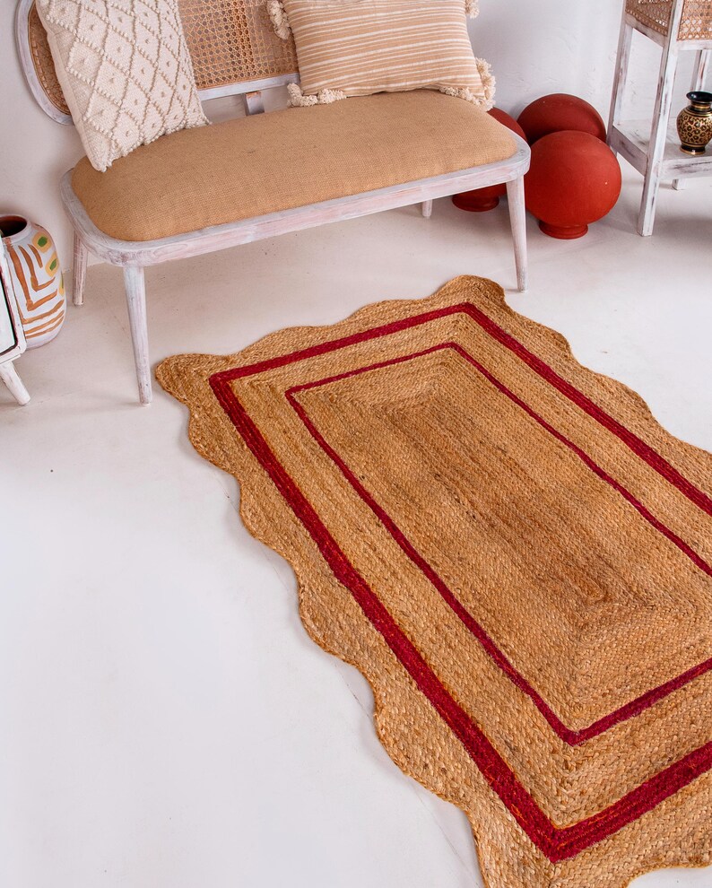 May include: A rectangular jute rug with a scalloped edge and two red stripes around the border.