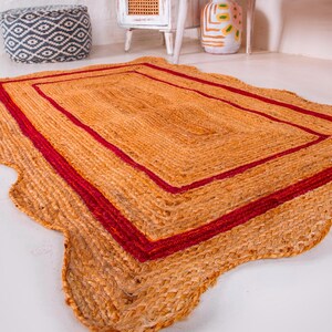 May include: A rectangular jute rug with a wavy edge and a double red border. The rug is made of natural fibers and has a rustic, earthy look.