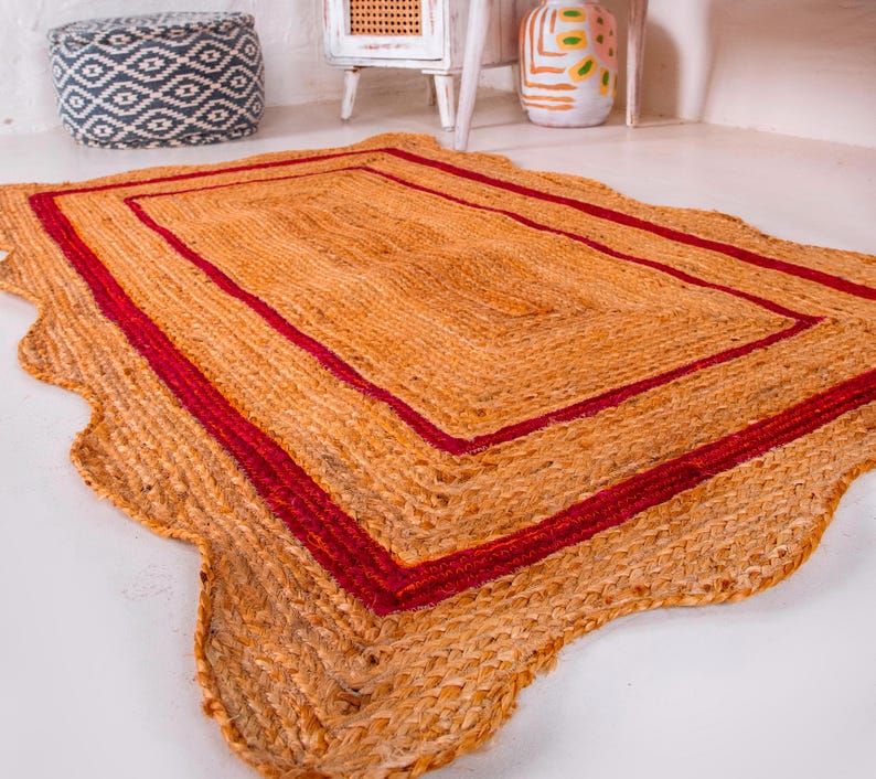 May include: A rectangular jute rug with a wavy edge and a double red border. The rug is made of natural fibers and has a rustic, earthy look.