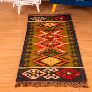 May include: A colorful, geometric patterned rug with a dark background and fringe edges. The rug has a traditional design with shades of green, orange, red, and yellow.