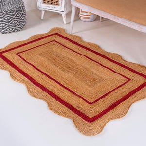 May include: A rectangular jute rug with a scalloped edge and a double red border. The rug is on a white floor.