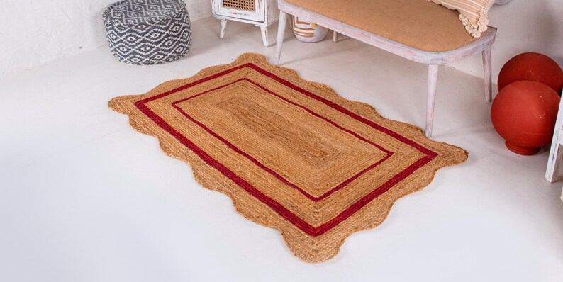 May include: A rectangular jute rug with a scalloped edge and a double red border. The rug is on a white floor.