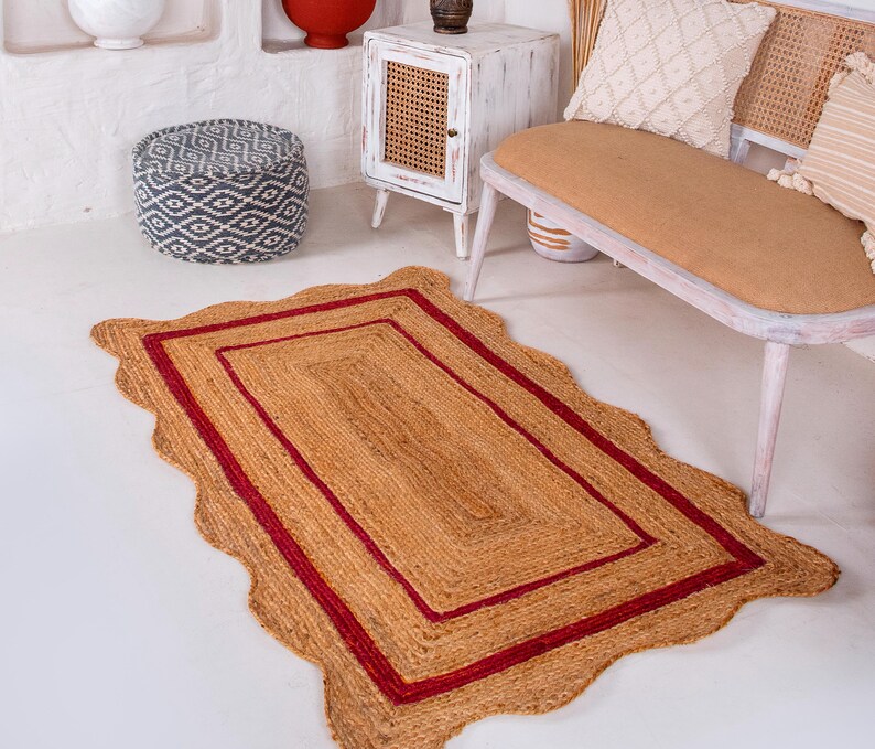 May include: A natural fiber rug with a wavy edge and a red border. The rug is made of jute and has a natural, earthy look.