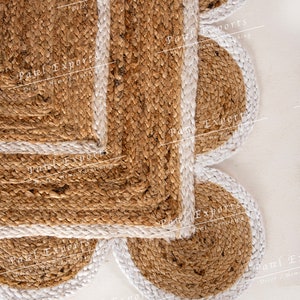 Op de afbeelding: Een bruin jute vloerkleed met een witte rand. Het vloerkleed is gemaakt van verschillende overlappende cirkels. Het vloerkleed heeft de tekst "Patel Exports Decor/Home Furnishing" erop gedrukt.