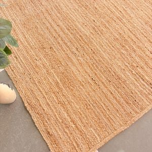 K&ouml;nnte beinhalten: Ein Naturfaser-Teppich aus Jute, einem nachhaltigen und strapazierf&auml;higen Material. Der Teppich hat eine hellbraune Farbe und eine gewebte Textur. Er ist perfekt, um jedem Raum einen Hauch von nat&uuml;rlicher Sch&ouml;nheit zu verleihen.