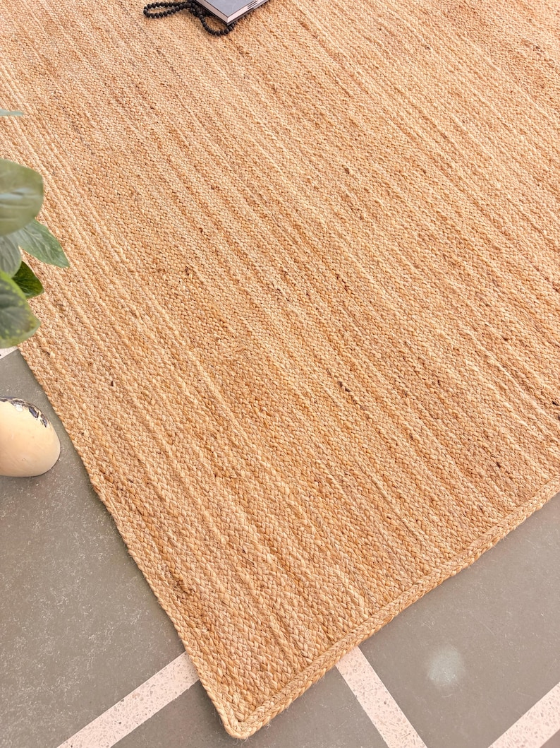K&ouml;nnte beinhalten: Ein Naturfaser-Teppich aus Jute, einem nachhaltigen und strapazierf&auml;higen Material. Der Teppich hat eine hellbraune Farbe und eine gewebte Textur. Er ist perfekt, um jedem Raum einen Hauch von nat&uuml;rlicher Sch&ouml;nheit zu verleihen.