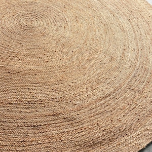 Könnte beinhalten: Ein runder Teppich aus natürlicher Jute mit gewebter Textur. Das Design des Teppichs zeigt konzentrische Kreise, die ein Spiralmuster bilden. Der Teppich hat eine warme, neutrale, beige Farbe, passend für verschiedene Einrichtungsstile.