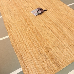 K&ouml;nnte beinhalten: Ein Naturfaser-Teppich aus Jute, einem nachhaltigen und strapazierf&auml;higen Material. Der Teppich hat eine hellbraune Farbe und eine gewebte Textur.