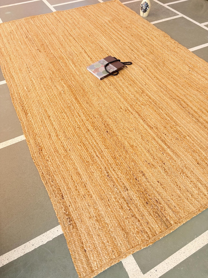 K&ouml;nnte beinhalten: Ein Naturfaser-Teppich aus Jute, einem nachhaltigen und strapazierf&auml;higen Material. Der Teppich hat eine hellbraune Farbe und eine gewebte Textur.