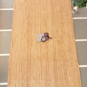 K&ouml;nnte beinhalten: Ein Naturfaser-Teppich aus Jute, einem nachhaltigen und strapazierf&auml;higen Material. Der Teppich hat eine hellbraune Farbe und eine gewebte Textur. Er ist perfekt, um jedem Raum einen Hauch von nat&uuml;rlicher Sch&ouml;nheit zu verleihen.