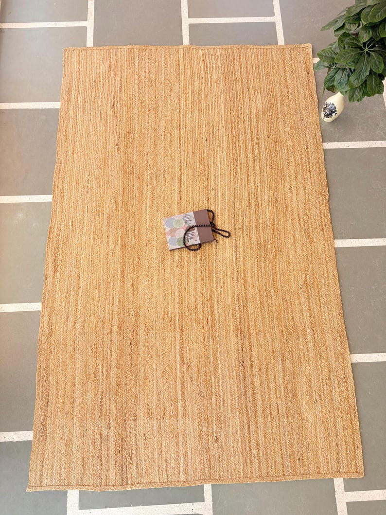 K&ouml;nnte beinhalten: Ein Naturfaser-Teppich aus Jute, einem nachhaltigen und strapazierf&auml;higen Material. Der Teppich hat eine hellbraune Farbe und eine gewebte Textur. Er ist perfekt, um jedem Raum einen Hauch von nat&uuml;rlicher Sch&ouml;nheit zu verleihen.