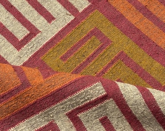 May include: Close-up of a woven textile with a geometric pattern. The design features alternating stripes of cream, burgundy, orange, and gold. The fabric has a textured appearance, suggesting a natural fiber construction. The pattern creates a sense of depth and visual interest.
