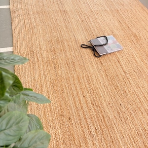 K&ouml;nnte beinhalten: Ein Naturfaser-Teppich aus Jute, einem nachhaltigen und strapazierf&auml;higen Material. Der Teppich hat eine hellbraune Farbe und eine gewebte Textur. Er ist perfekt, um jedem Raum einen Hauch von nat&uuml;rlicher Sch&ouml;nheit zu verleihen.