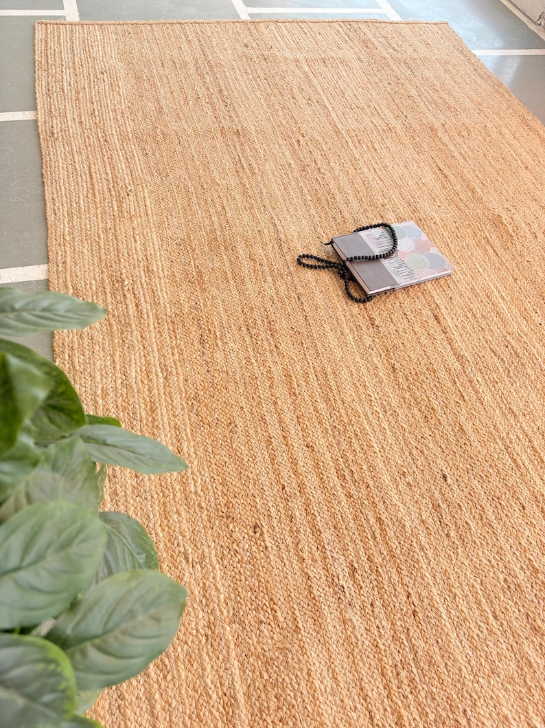 K&ouml;nnte beinhalten: Ein Naturfaser-Teppich aus Jute, einem nachhaltigen und strapazierf&auml;higen Material. Der Teppich hat eine hellbraune Farbe und eine gewebte Textur. Er ist perfekt, um jedem Raum einen Hauch von nat&uuml;rlicher Sch&ouml;nheit zu verleihen.