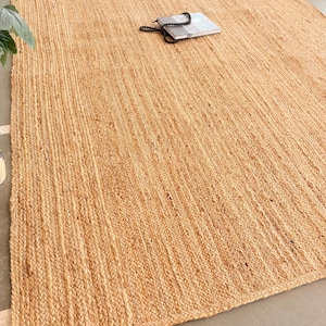 K&ouml;nnte beinhalten: Ein Naturfaser-Teppich aus Jute, einem nachhaltigen und strapazierf&auml;higen Material. Der Teppich hat eine hellbraune Farbe und eine gewebte Textur. Er ist perfekt, um jedem Raum einen Hauch von nat&uuml;rlicher Sch&ouml;nheit zu verleihen.