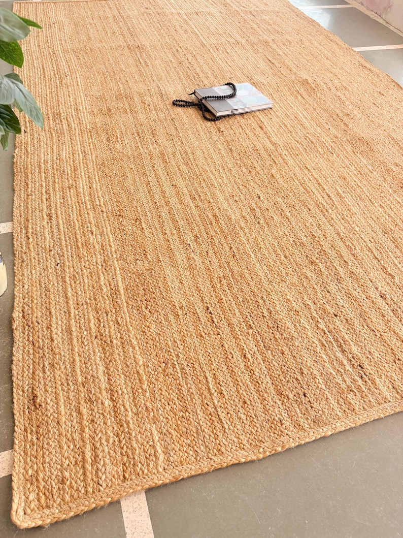 K&ouml;nnte beinhalten: Ein Naturfaser-Teppich aus Jute, einem nachhaltigen und strapazierf&auml;higen Material. Der Teppich hat eine hellbraune Farbe und eine gewebte Textur. Er ist perfekt, um jedem Raum einen Hauch von nat&uuml;rlicher Sch&ouml;nheit zu verleihen.