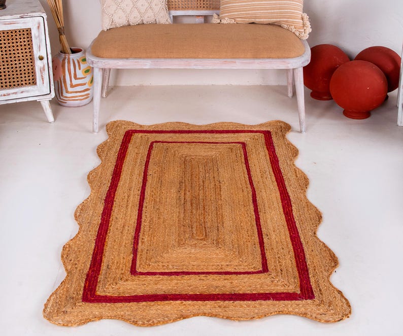 May include: A natural fiber rug with a red border and a wavy edge. The rug is made of jute and has a natural, earthy color.
