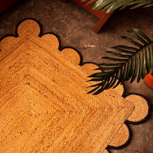 Peut inclure: Un tapis en fibres naturelles avec un bord festonné. Le tapis est tissé dans une couleur brune naturelle et a une bordure noire. Le tapis est sur un sol brun.