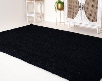May include: A black woven rug with a textured surface. The rug is laid out on a white floor.